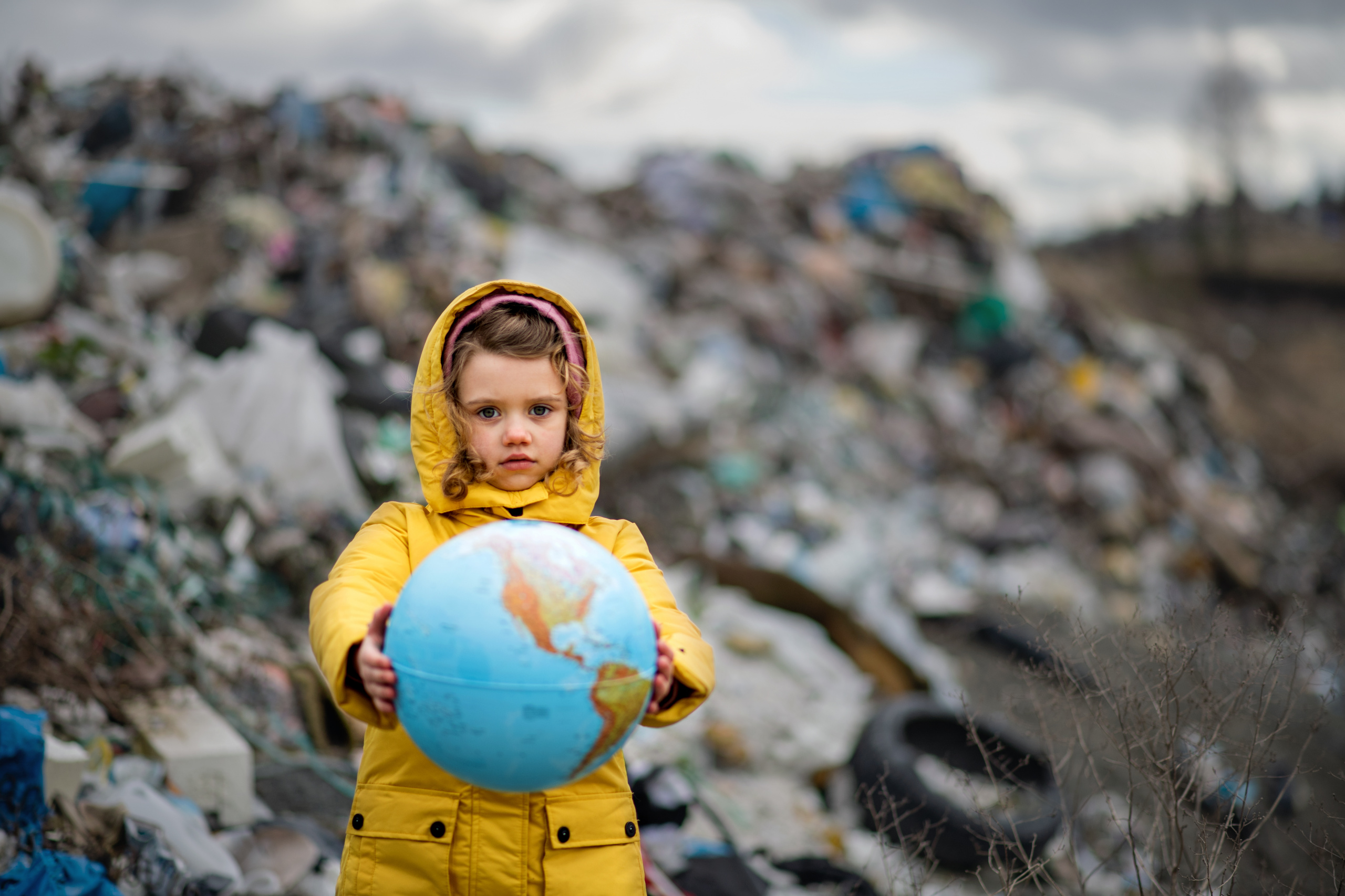 Ein Mädchen mit einer Weltkugel steht vor einer Müllhalde